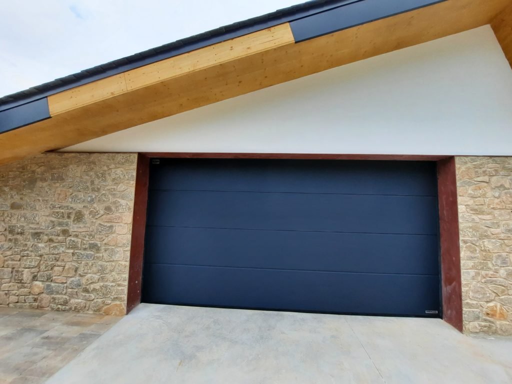 Puerta seccional antracita instalada en garaje con fachada de piedra