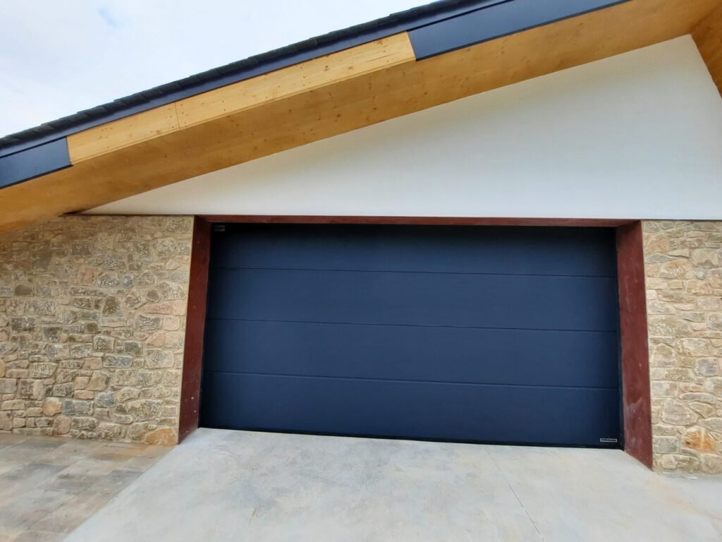 Puerta seccional antracita instalada en garaje con fachada de piedra